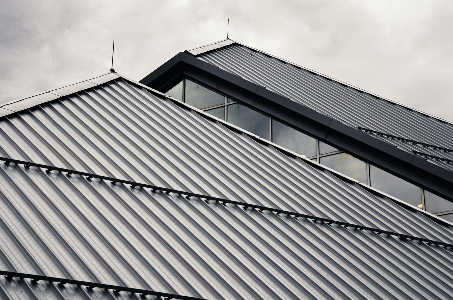 Dark gray metal roof panels with snow guard rails under a cloudy sky