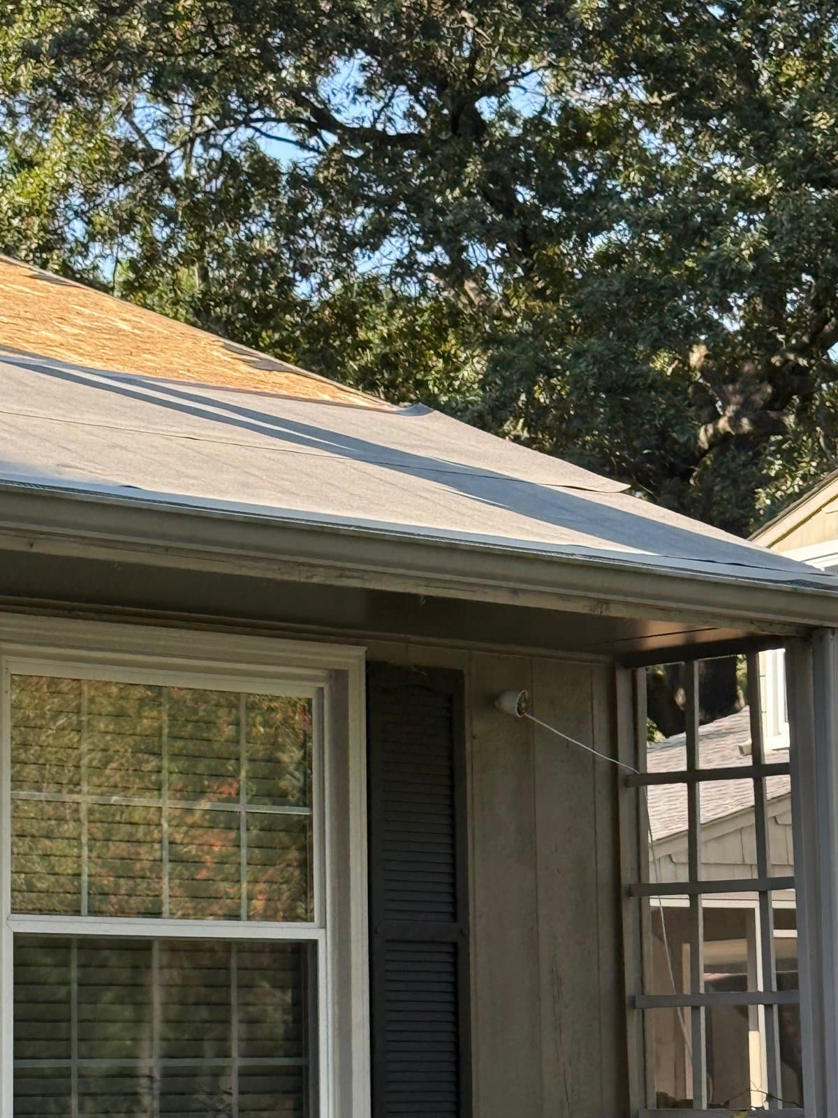 Underlayment laid across the lower roof above a porch, with exposed wood decking farther up the slope