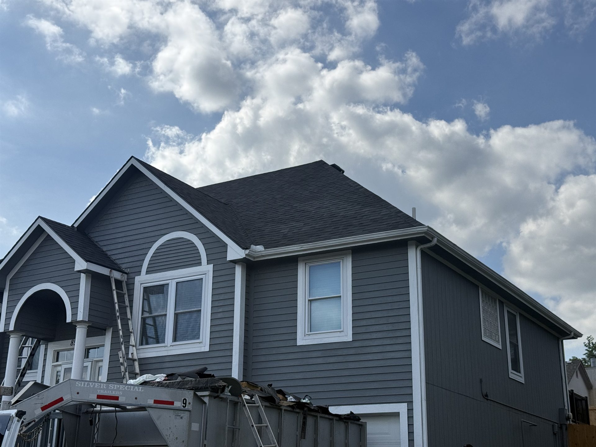 Gray-sided home with dark shingle rooflines, arched white trim, and a ladder at the roof edge