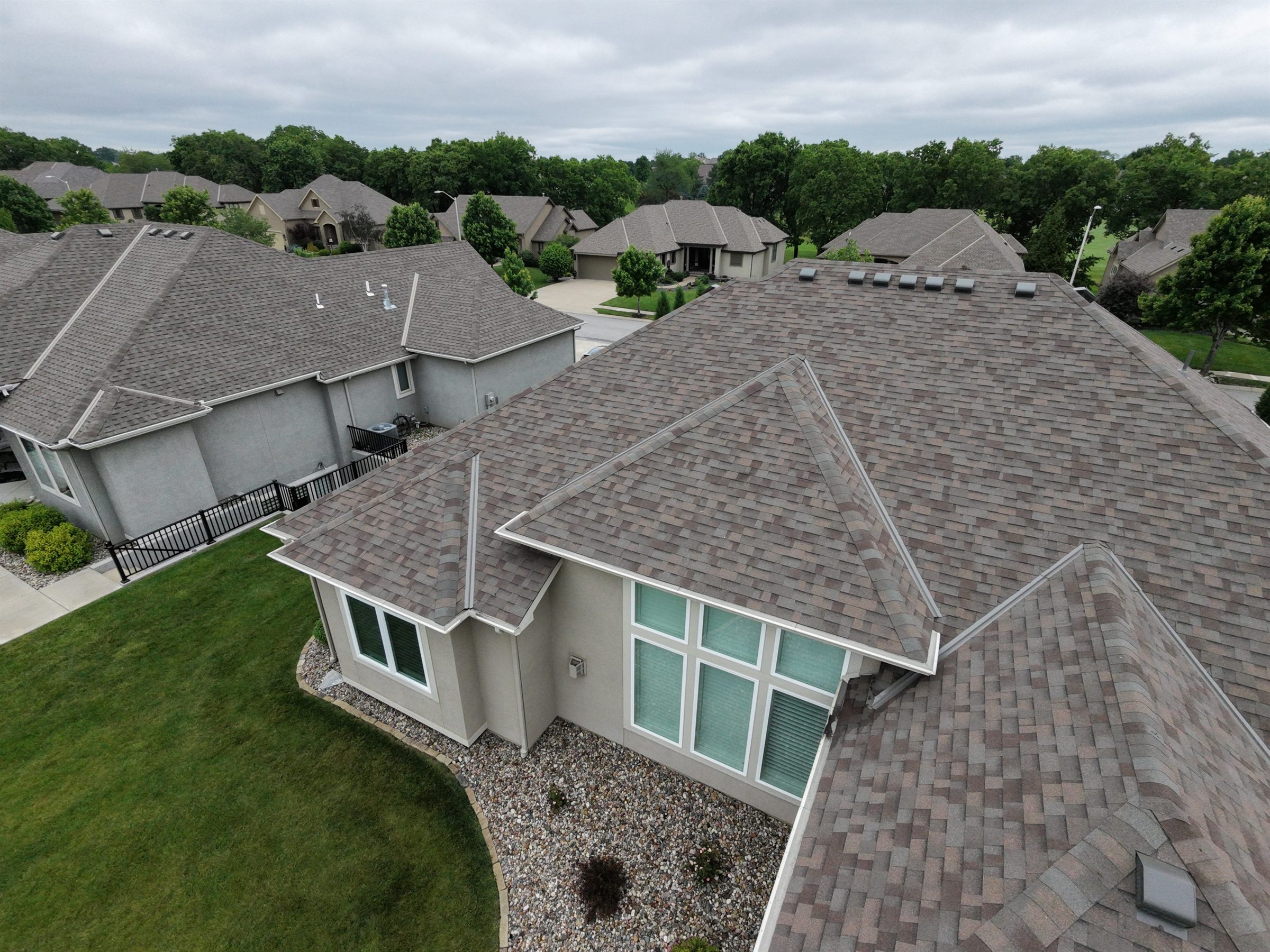 Aerial view of a shingle roof with intersecting ridges above a beige home