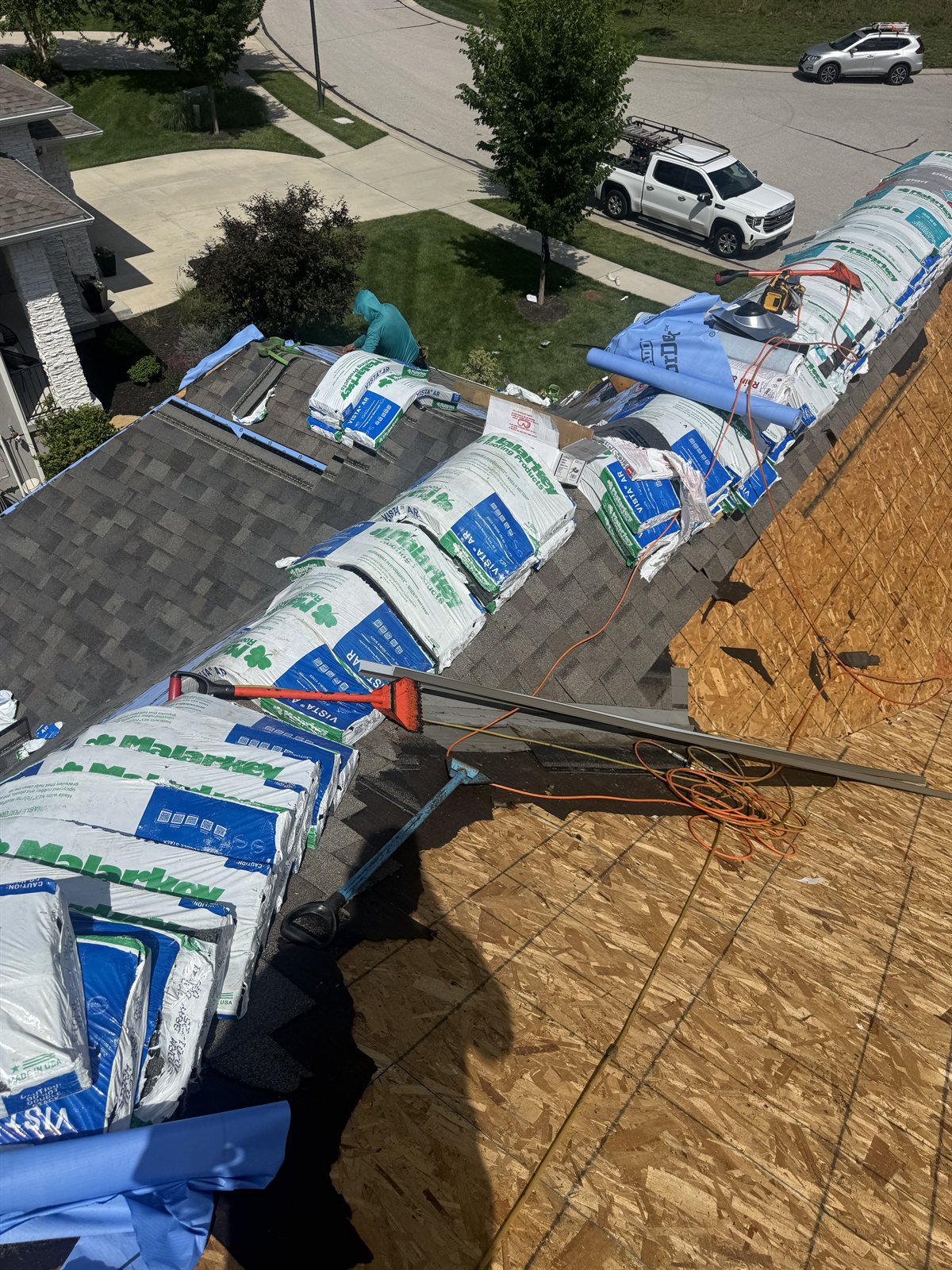 Shingle bundles and tools staged beside exposed roof decking