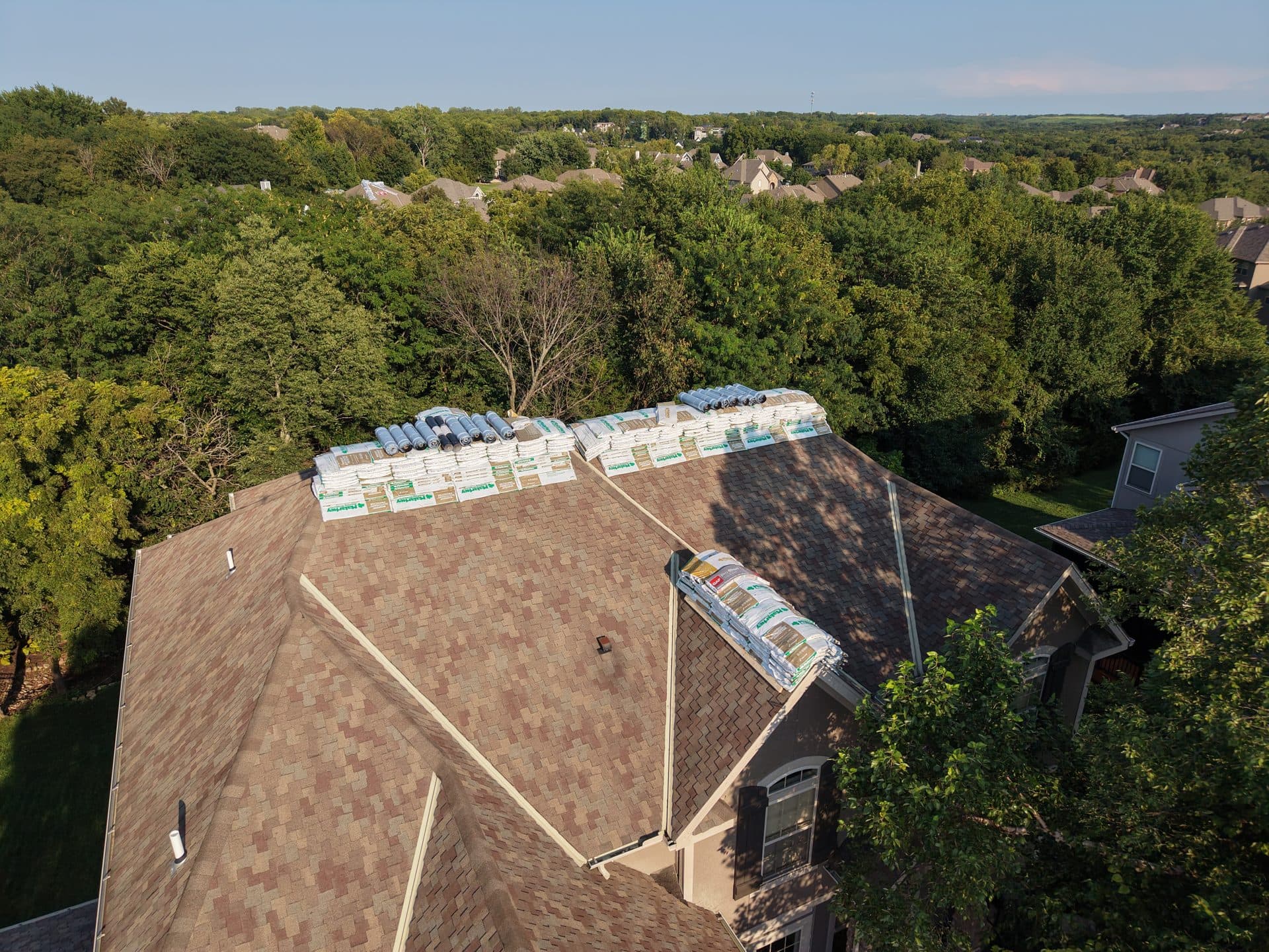 Drone view of shingle bundles staged on the ridge of an Olathe, KS home before a roof replacement