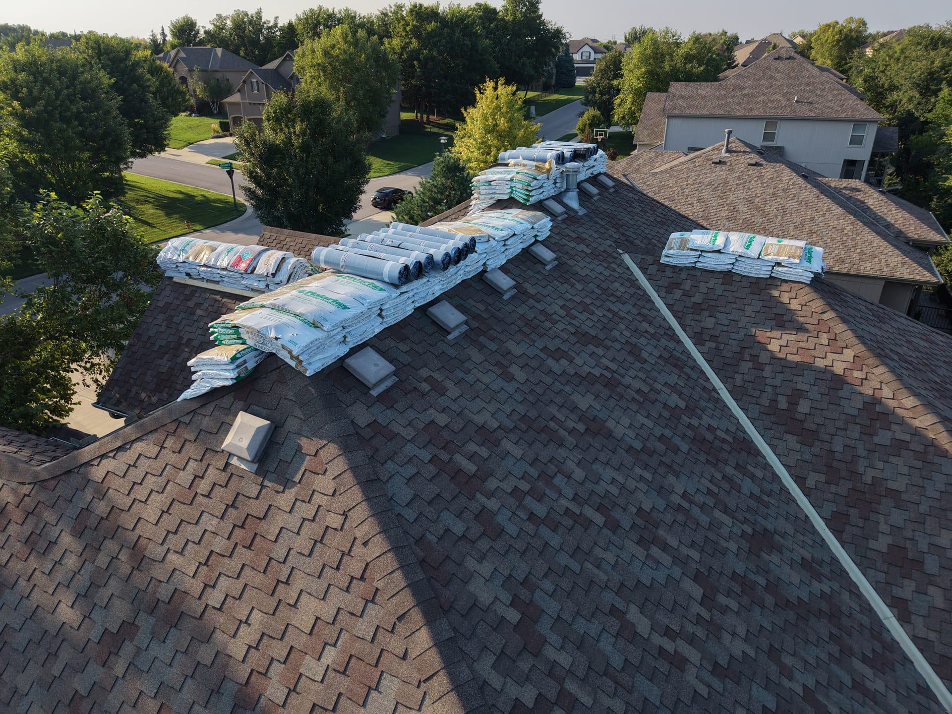 Shingle bundles and underlayment rolls loaded onto an Olathe, KS roof ahead of tear-off