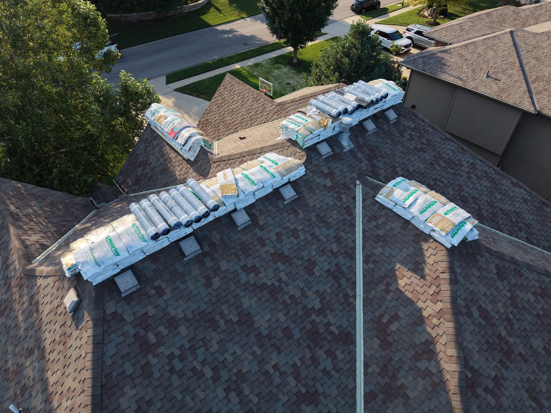 Aerial view of roofing materials staged across the ridges of a two-story Olathe, KS home