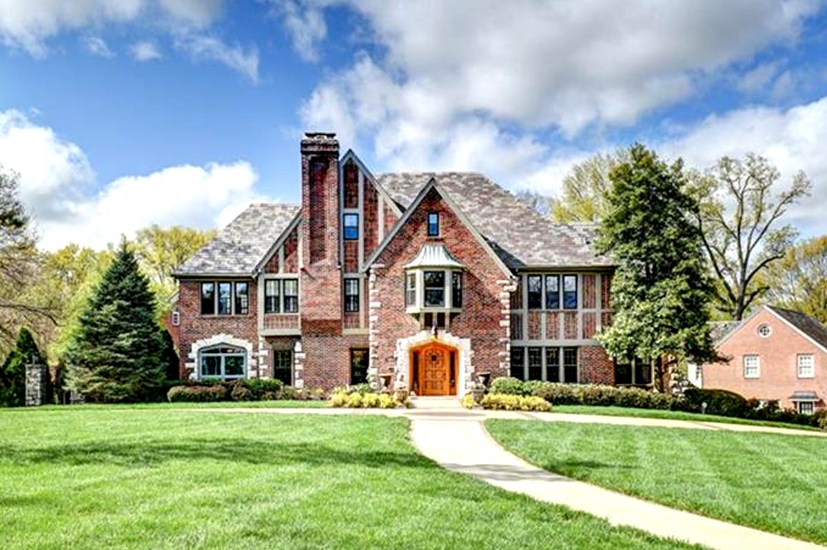 A brick Tudor-style home with steep gables and a wide front lawn