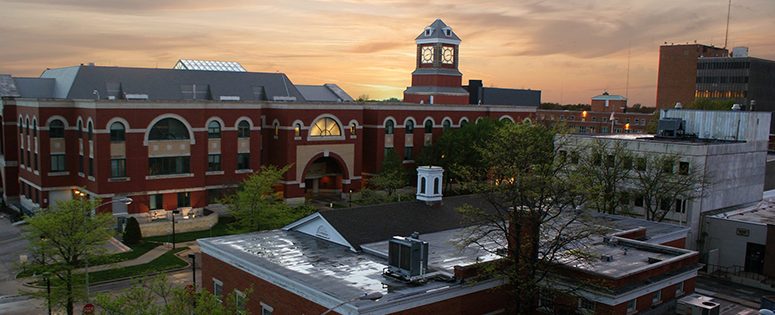 The clock tower of Olathe City Hall at sunset, above neighboring downtown rooftops