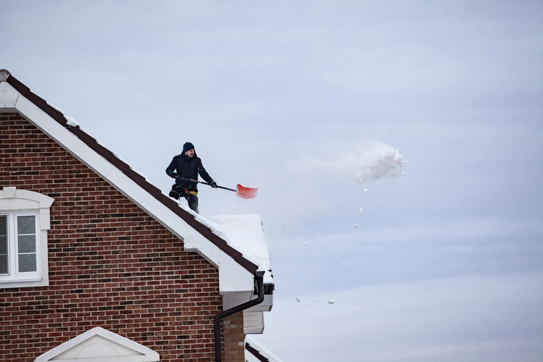 Homeowner using a roof rake to remove snow from eaves while standing on the ground