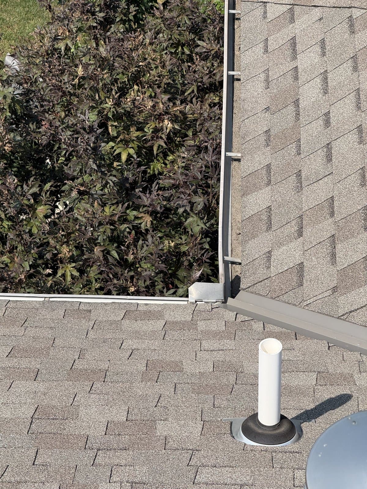 White vent pipe with a flashing boot beside an open metal valley on a shingle roof